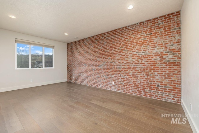 unfurnished room featuring brick wall, a textured ceiling, baseboards, and wood finished floors