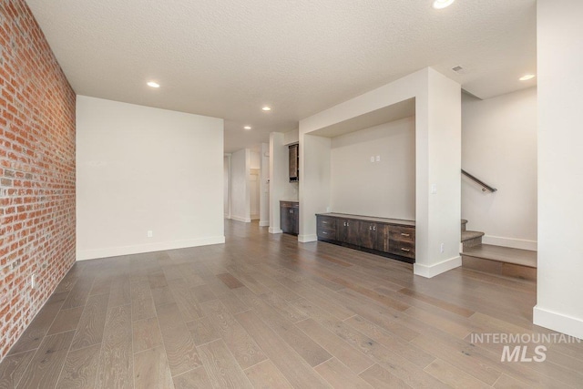 unfurnished living room featuring brick wall, baseboards, stairway, wood finished floors, and a textured ceiling