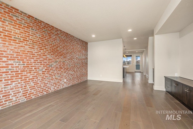 unfurnished room featuring dark wood-type flooring, a textured ceiling, recessed lighting, brick wall, and baseboards