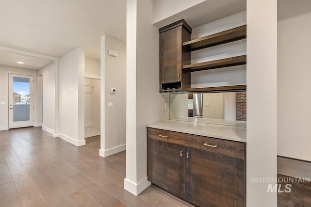 interior space with wood finished floors, baseboards, open shelves, light countertops, and dark brown cabinetry