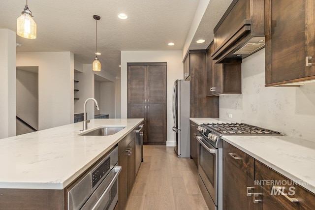 kitchen with a sink, dark brown cabinetry, light wood-style floors, appliances with stainless steel finishes, and decorative light fixtures