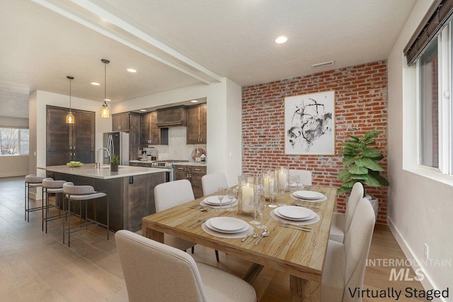 dining area with baseboards, wood finished floors, a textured ceiling, and brick wall