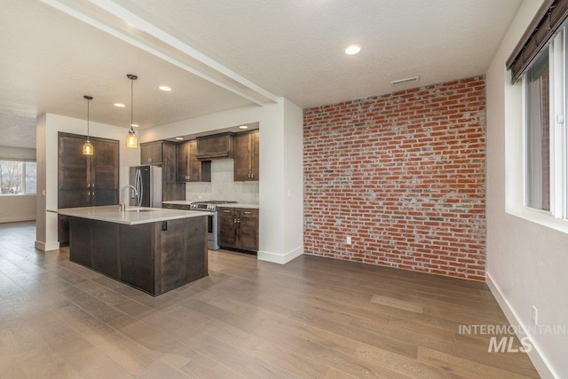 kitchen with brick wall, light countertops, dark wood-type flooring, dark brown cabinets, and appliances with stainless steel finishes