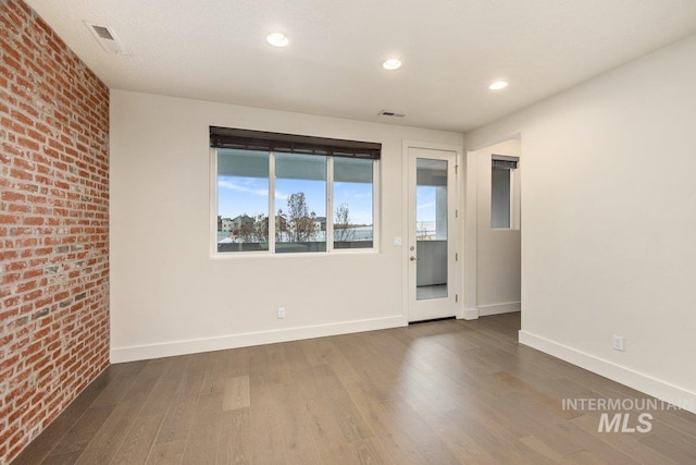 spare room featuring visible vents, baseboards, wood finished floors, and brick wall