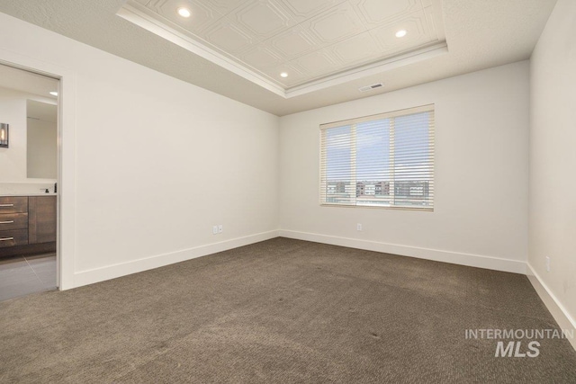 spare room featuring a tray ceiling, baseboards, visible vents, and dark carpet