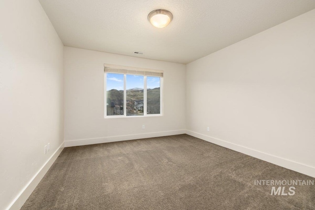 empty room featuring carpet flooring, baseboards, visible vents, and a textured ceiling