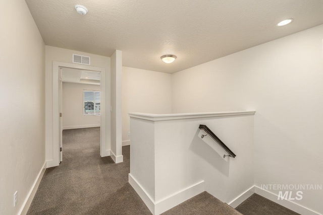 corridor featuring an upstairs landing, visible vents, dark carpet, and baseboards