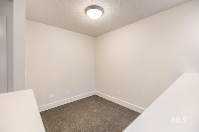 empty room featuring baseboards, a textured ceiling, and dark carpet