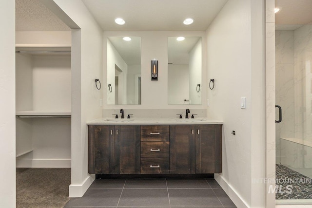 bathroom featuring double vanity, baseboards, a marble finish shower, and a sink