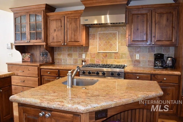 221 Picabo Street #D, Interest 1-H, Ketchum, ID 83340 - kitchen with wall chimney range hood, a sink, light stone counters, an island with sink, and glass insert cabinets