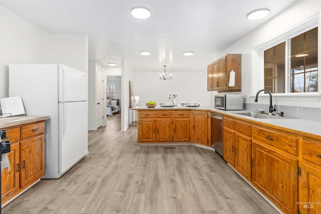 kitchen featuring a sink, light countertops, appliances with stainless steel finishes, a peninsula, and brown cabinets