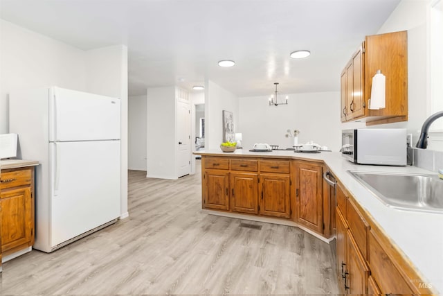 kitchen featuring light countertops, a peninsula, freestanding refrigerator, and a sink