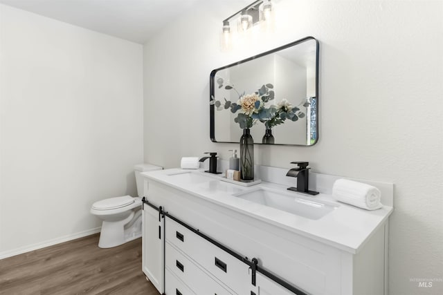 bathroom featuring double vanity, a sink, toilet, and wood finished floors