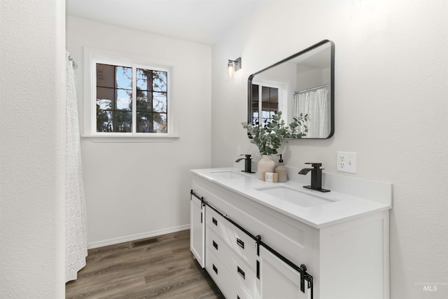 full bath featuring wood finished floors, double vanity, a sink, and visible vents