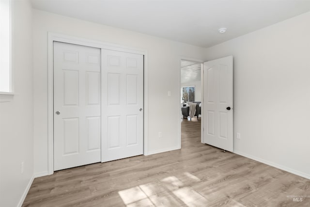 unfurnished bedroom featuring a closet, light wood-style flooring, baseboards, and multiple windows