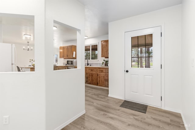 entryway featuring light wood finished floors, a notable chandelier, baseboards, and a healthy amount of sunlight