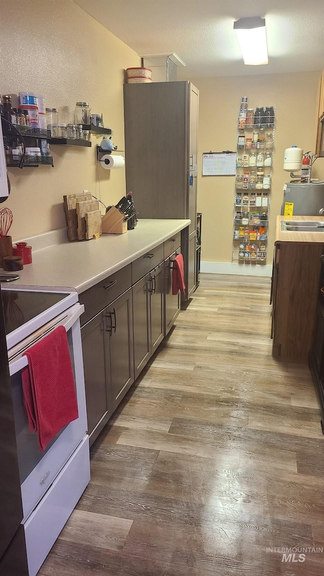 kitchen with electric stove, light wood finished floors, light countertops, and a sink