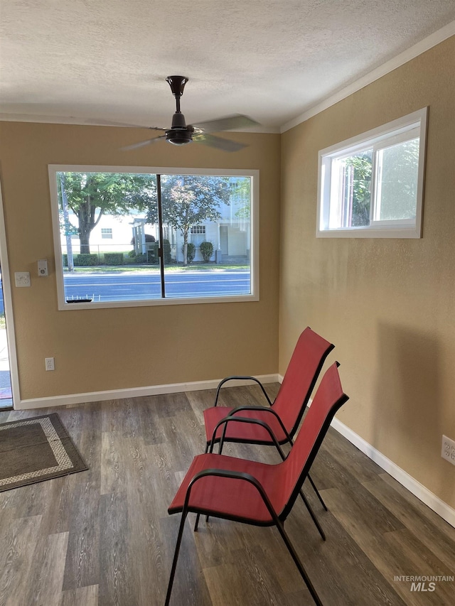 living area with a textured ceiling, wood finished floors, ceiling fan, crown molding, and baseboards