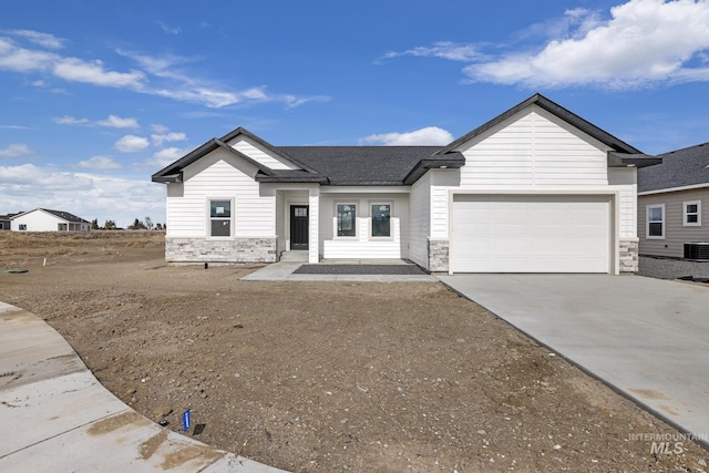 view of front of house with a garage, central AC, stone siding, concrete driveway, and roof with shingles