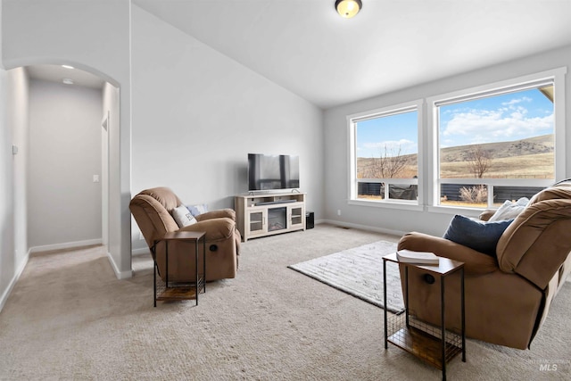 living area featuring baseboards, arched walkways, carpet, and vaulted ceiling