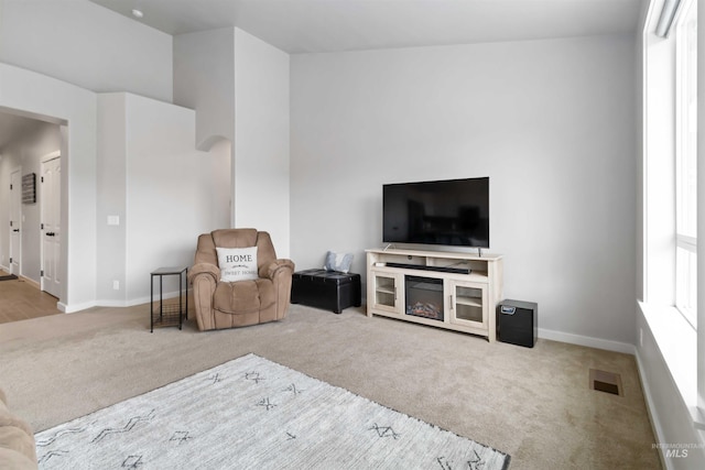 living area featuring visible vents, carpet floors, arched walkways, and baseboards