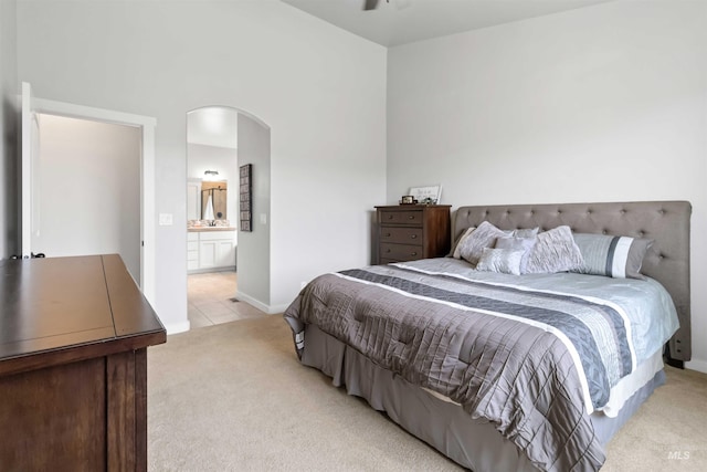 bedroom featuring ensuite bath, light tile patterned floors, arched walkways, and light carpet