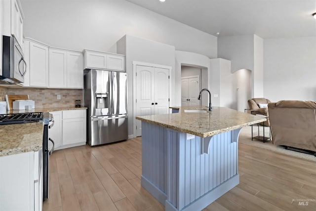 kitchen featuring open floor plan, light wood-style flooring, appliances with stainless steel finishes, arched walkways, and a sink