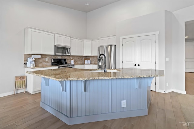 kitchen featuring tasteful backsplash, appliances with stainless steel finishes, white cabinets, and light wood finished floors