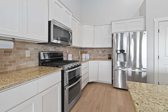 kitchen featuring light wood finished floors, backsplash, appliances with stainless steel finishes, and white cabinetry