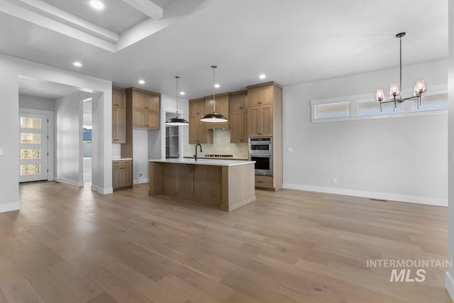 kitchen with an inviting chandelier, double oven, a center island with sink, decorative light fixtures, and light wood-type flooring