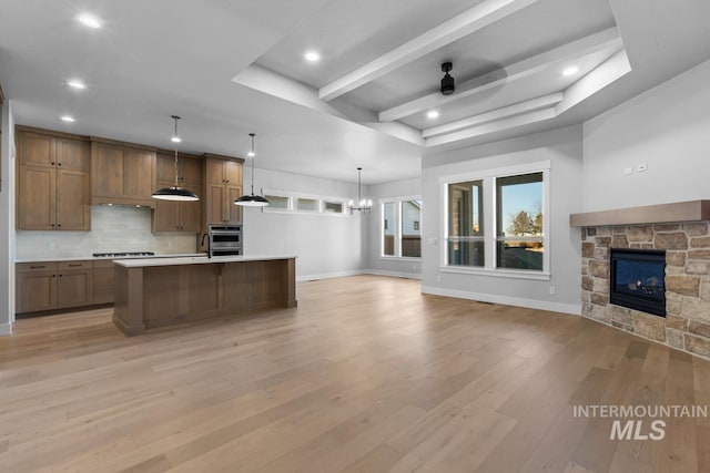 kitchen featuring light hardwood / wood-style flooring, a stone fireplace, stovetop, ceiling fan with notable chandelier, and decorative light fixtures