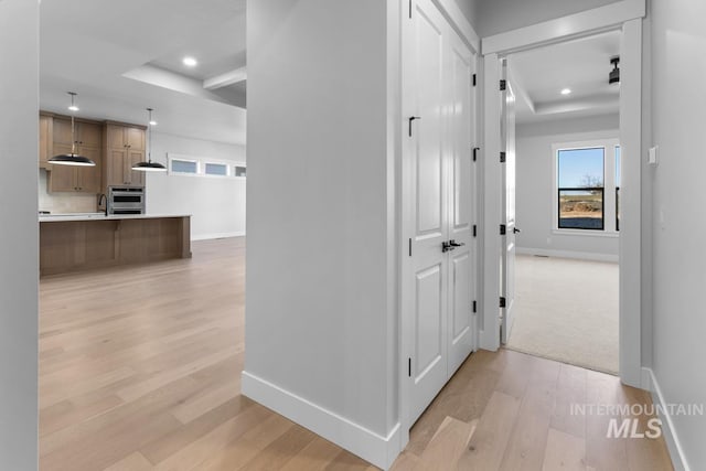 hall with sink, a raised ceiling, and light wood-type flooring