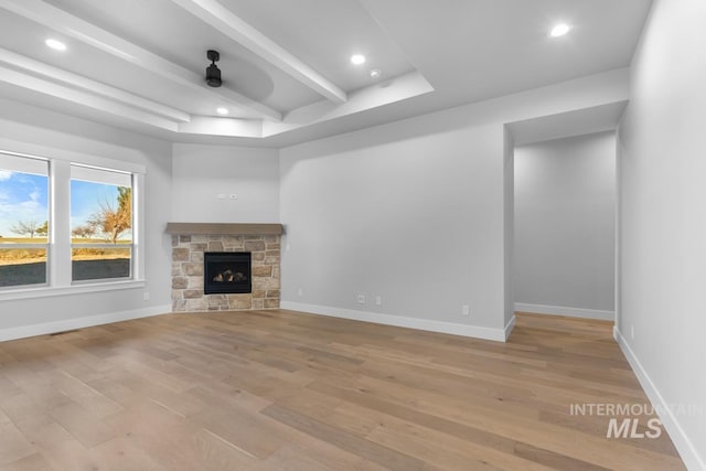 unfurnished living room with ceiling fan, a fireplace, beam ceiling, and light hardwood / wood-style flooring