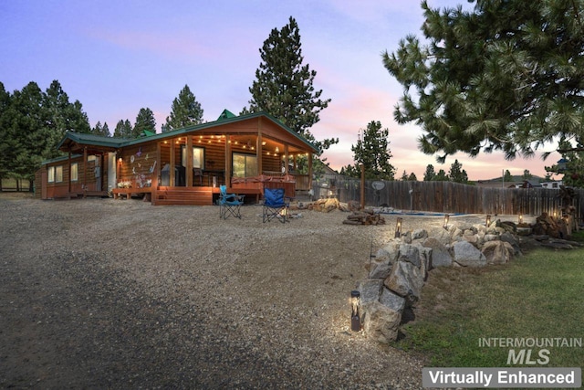 back of house at dusk with a wooden deck, fence, and log veneer siding