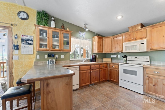 kitchen featuring a sink, a peninsula, glass insert cabinets, a breakfast bar, and white appliances