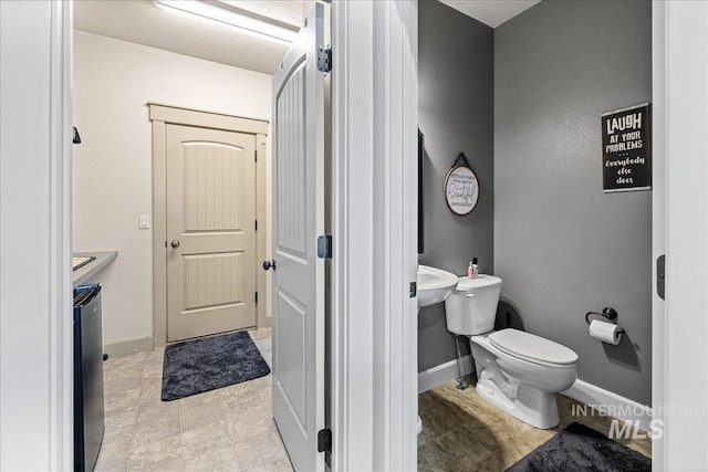1063 Hitchcock St, Meridian, ID 83646 - bathroom featuring a textured wall, toilet, baseboards, and a sink