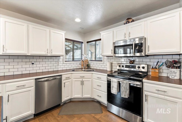 kitchen with stainless steel appliances, sink, white cabinets, and light wood-type flooring