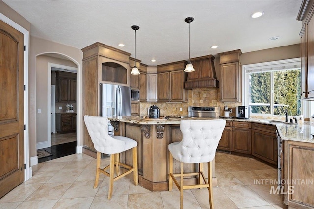 kitchen featuring appliances with stainless steel finishes, custom exhaust hood, light stone counters, a kitchen island, and decorative light fixtures