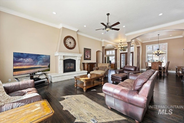 living room with ceiling fan with notable chandelier, dark wood-type flooring, crown molding, and ornate columns