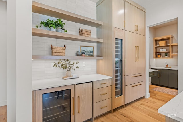 kitchen with backsplash, light stone countertops, light brown cabinetry, beverage cooler, and light wood-type flooring