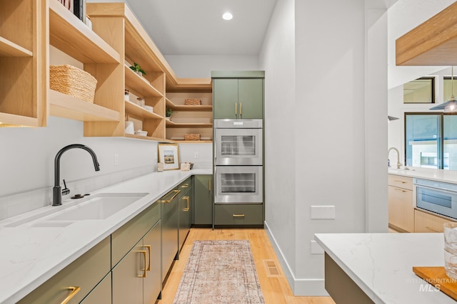 kitchen with sink, light stone counters, light hardwood / wood-style floors, green cabinetry, and stainless steel double oven