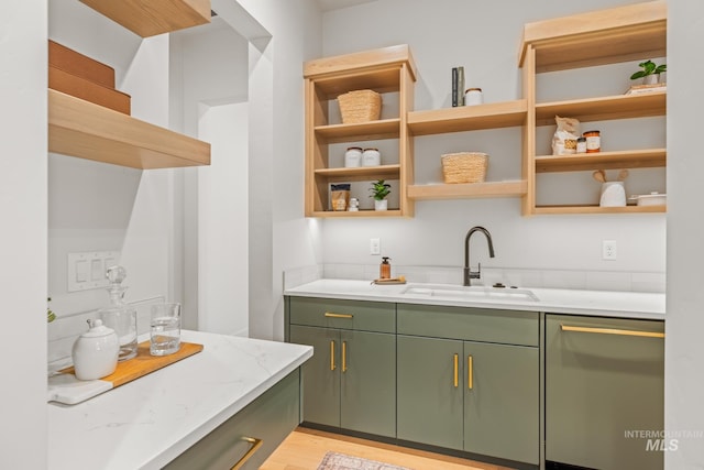 kitchen with sink, light stone counters, light hardwood / wood-style flooring, stainless steel dishwasher, and green cabinets