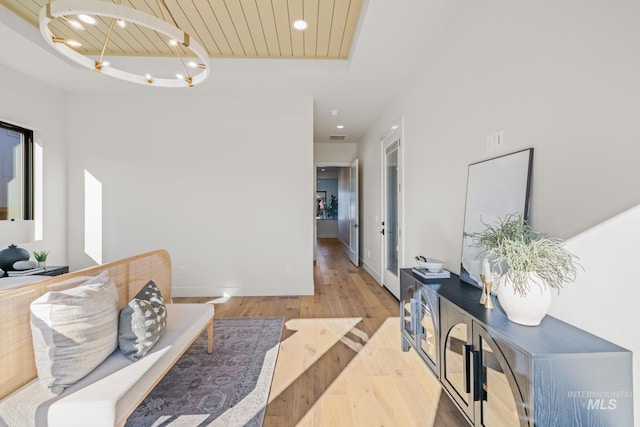 hallway featuring an inviting chandelier, wooden ceiling, a raised ceiling, and light wood-type flooring