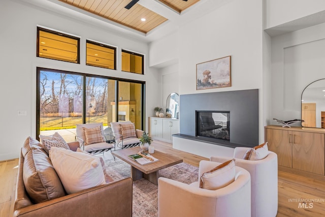 living room with coffered ceiling, a towering ceiling, light hardwood / wood-style flooring, and beamed ceiling