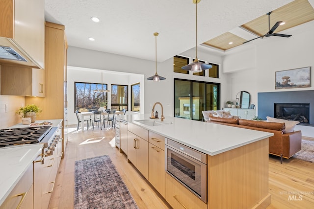 kitchen featuring an island with sink, decorative light fixtures, light brown cabinetry, and sink