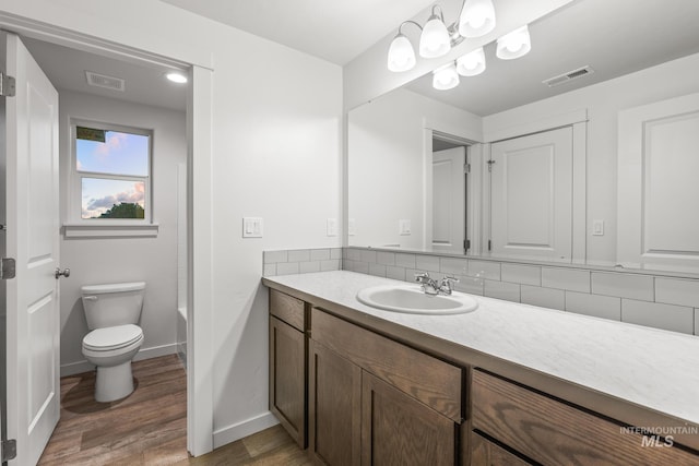 bathroom featuring hardwood / wood-style flooring, decorative backsplash, toilet, and vanity