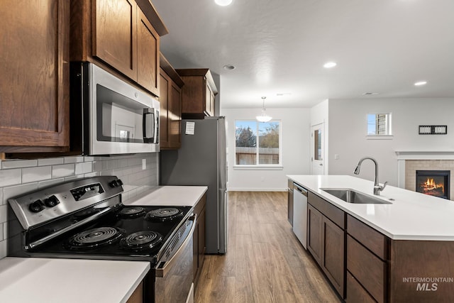 kitchen with sink, backsplash, hardwood / wood-style floors, decorative light fixtures, and appliances with stainless steel finishes