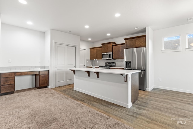 kitchen with a breakfast bar area, hardwood / wood-style flooring, built in desk, an island with sink, and stainless steel appliances