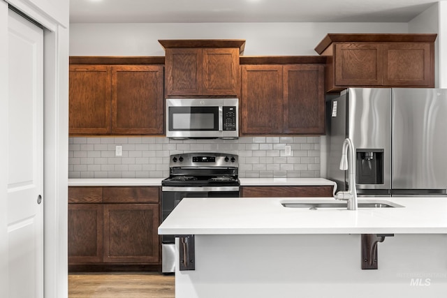 kitchen with a kitchen breakfast bar, backsplash, stainless steel appliances, sink, and light hardwood / wood-style floors