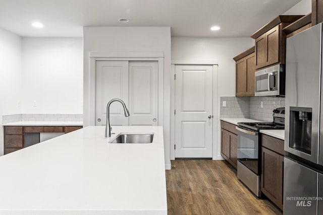 kitchen with appliances with stainless steel finishes, tasteful backsplash, dark wood-type flooring, sink, and a center island with sink